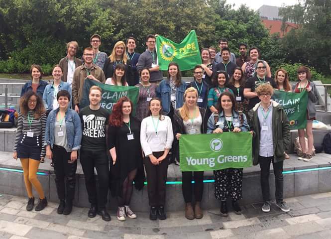 A large group of Young Greens holding official Young Greens, Federation of Young European Greens, and Climate Sense flags.