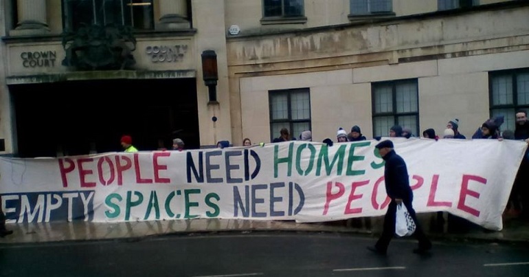 Group of people holding a banner reading "people need homes, empty spaces need people"