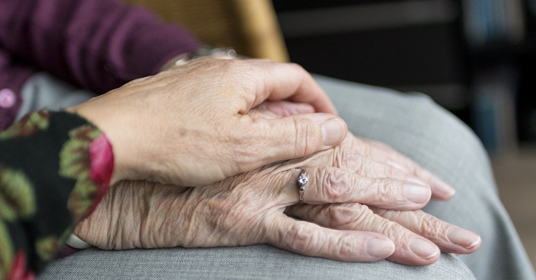 One person's hand comforting another in a care home