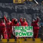 Reclaim the Power activists stood on mining equipment at an open cast coal mine, their banner reads Leeds Reclaim the Power.