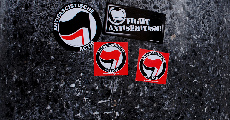 Stickers on a bollard reading "Fight antisemitism" and "antifascistiche actie"