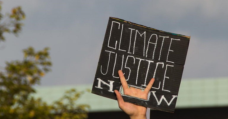 A photo of a hand holding a placard reading "Climate Justice Now"