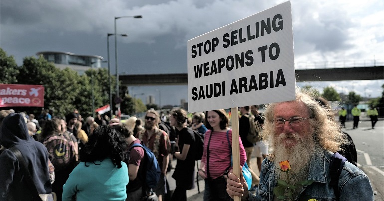 A photo of campaigners at a protest against the arms trade. One is holding a sign reading "stop selling weapons to Saudi Arabia"