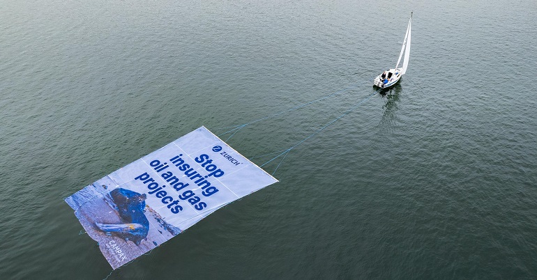 A photo of a boat pulling a floating banner that reads: "Zurich: Stop insuring oil and gas projects"