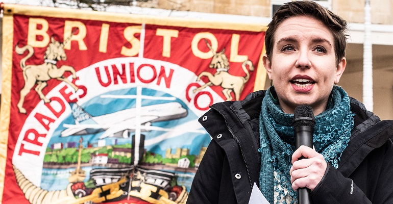 Carla Denyer speaking at a People's Assembly demonstration with a Bristol Trades Union Council banner behind her