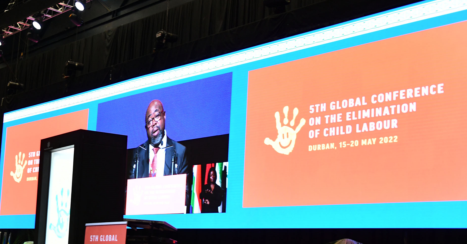 A photo of the screens at the International Labour Organisation’s 5th Global Conference on Elimination of Child Labour, displaying the logo of the event and a speaker addressing the conference
