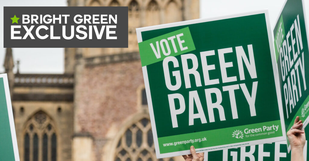 A photo of a Green Party placard in front of Westminster, with an overlay which reads "Bright Green Exclusive"
