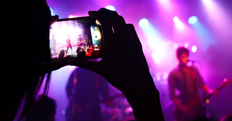 A photo of a live music event. An attendee is taking a photo of the stage on a mobile phone