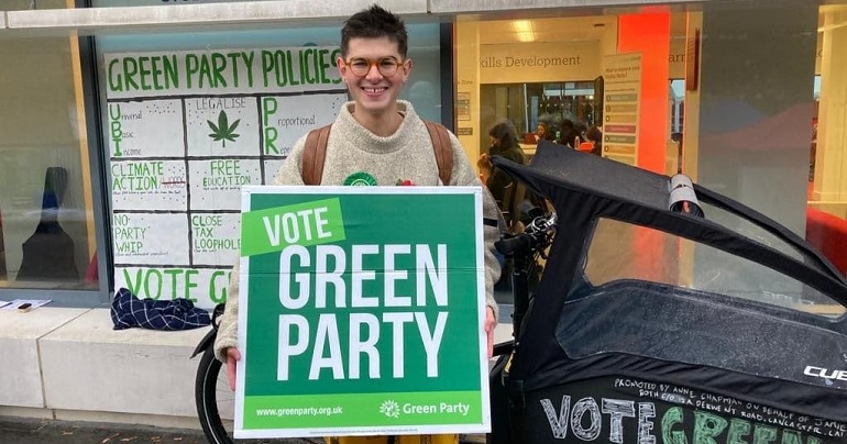 A photo of Jamie Payne holding a placard reading "Vote Green Party"