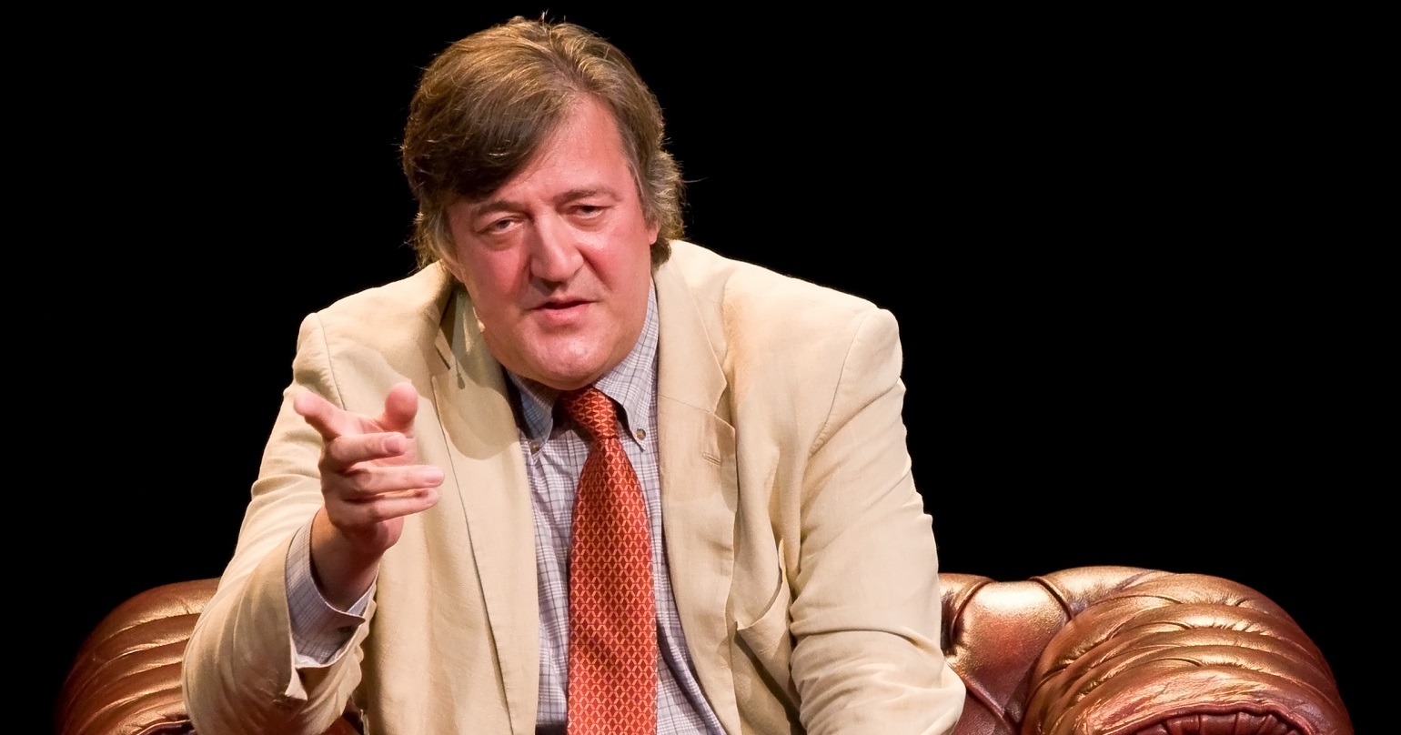 Stephen Fry in an armchair pointing