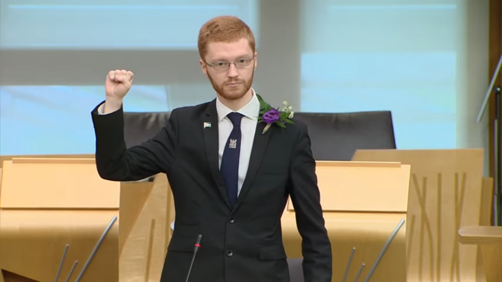 Ross Greer in the Scottish Parliament with his fist raised