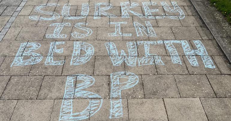 A photo of chalk at the university of Surrey reading "Surrey is in bed with BP"